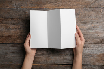 Woman with blank brochure on wooden background, above view. Mock up for design
