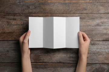Woman with blank brochure on wooden background, above view. Mock up for design