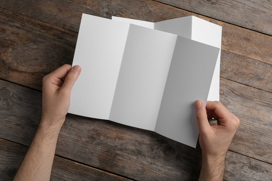 Man with blank brochure on wooden background, above view. Mock up for design