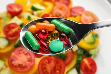 Spoon with weight loss pills over plate with vegetable salad, closeup