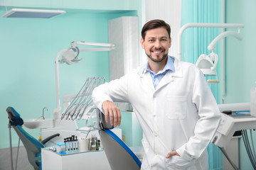 Professional male dentist in white coat at workplace. Space for text