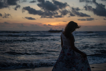 Young dresses woman standing on beach in ocean at sunset