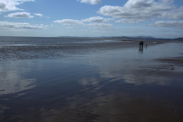 Naklejka premium Family walking with a dog on a wet beach at Southerness, Dumfries ang Galloway, Scotland..