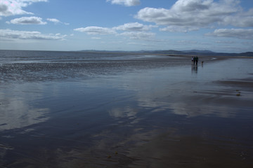 Family walking with a dog on a wet beach at Southerness, Dumfries ang Galloway, Scotland..