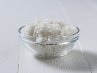 Glass bowl with long grain rice on white wooden table.