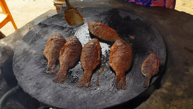 A woman flipping the fishes being fried in a big pan
