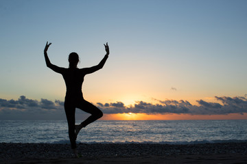 Fototapeta premium silhouette of person doing yoga on the beach at sunrise