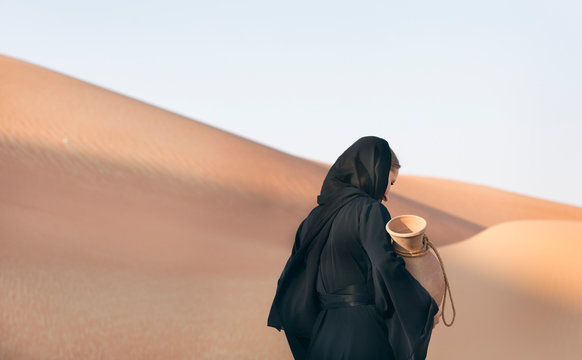 woman in abaya (emirati traditional dress) in a desert with water dish