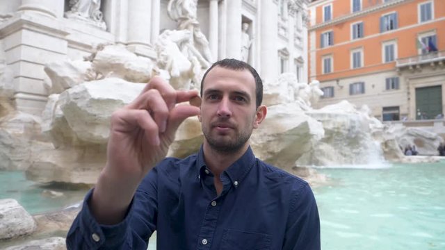 Tourist Holding Up A Coin With The Trevi Fountain In The Background.