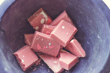 Broken and shattered pieces of ruby red chocolate in a round charcoal stone ceramic bowl. White and brwon background. Speckled chocolate.