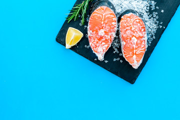Raw salmon fish on black plates for cooking steaks on blue restaurant kitchen background top view space for text