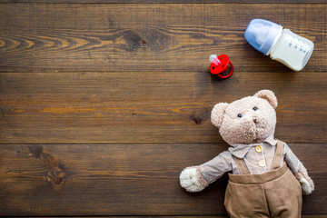 Craft toys for kids. Handmade teddy bear, dummy and baby bottle with milk. Wooden background top view mock up