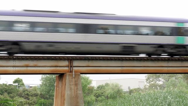 Passenger train moving over a rusty bridge passing over a river on a rainy summers day.