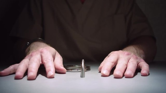 Close-up shot that slowly dollies in on a prisoner's hands, cuffed to a table in an interrogation room.