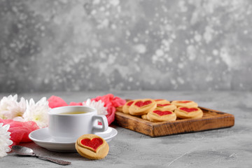 White cup and cookies with hearts on a gray background. Beautiful still life, the mood of Valentine's Day. Space under the text.