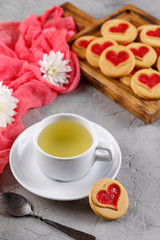 White cup of green tea and cookies with hearts on a gray background. Beautiful still life, the mood of Valentine's Day.