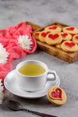 A cup of green tea and cookies with hearts on a gray background. Beautiful still life, the mood of Valentine's Day.