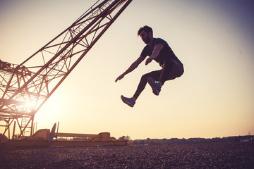 Young man exercising outdoors by the crane at sunset
