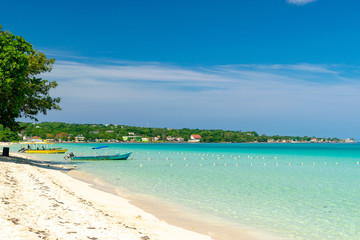 Sunny day along the Seven Mile Beach in tropical Negril, Jamaica. Tour boats await passengers and caucasian tourists in the water at a distance.