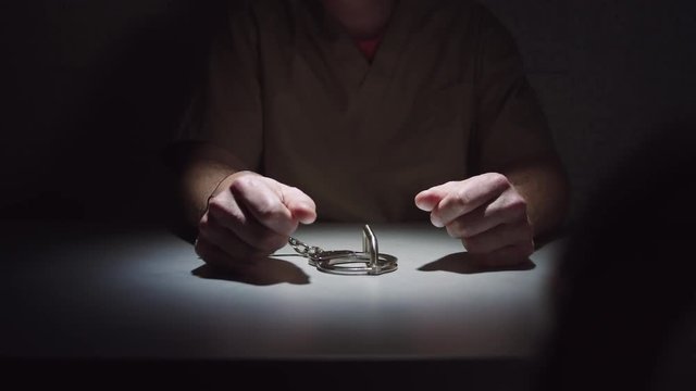 Medium tracking shot of a prisoner as he sits handcuffed in an interrogation room.