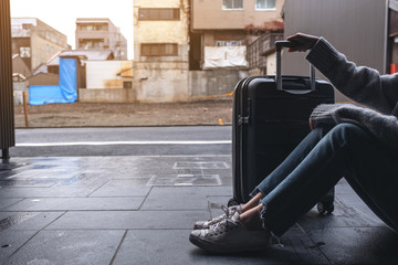 Closeup image of a woman sitting and holding a black baggage for traveling in the outdoors