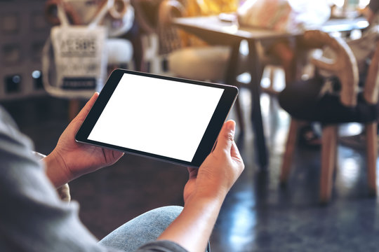 Mockup image of a woman holding black tablet pc with blank white screen horizontally while sitting in cafe