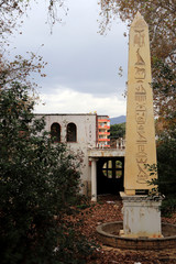 Abandoned park with a pillar with Egyptian hieroglyphs and a ruined building in the background