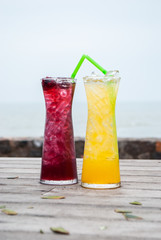Juice mix berry, mango and passion fruit drink in tall glass with straw green color on wooden terrace front of sea