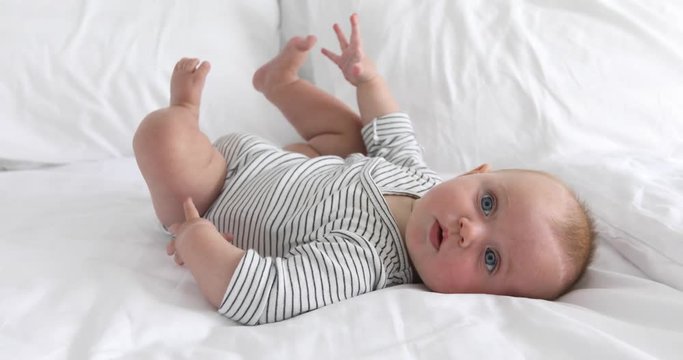 Side view of adorable little baby lying on white soft blanket on bed daylight