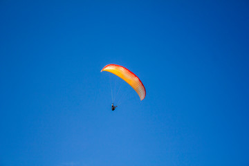 man on a red yellow white paraglide in a clear blue sky