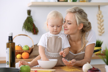 Happy mother and little daughter cooking in kitchen. Spending time all together, family fun concept