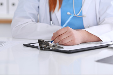 Fototapeta premium Close up of a female doctor filling up an application form while sitting at the table