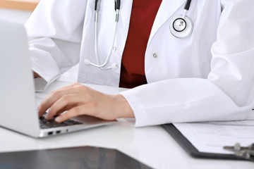 Close-up of unknown female doctor typing on laptop computer while sitting  at the table