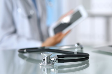 Stethoscope lying on glass desk with laptop computer at busy physician background. Medicine or pharmacy concept. Medical tools at doctor working table