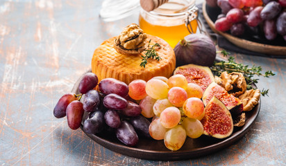 Cheese plate served with grapes, jam, figs, crackers and nuts on a background.