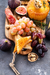 Cheese plate served with grapes, jam, figs, crackers and nuts on a background.