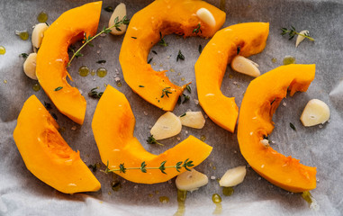 Sliced pumpkin with greens and sea salt on white baking paper as background. Top view. Copy space.