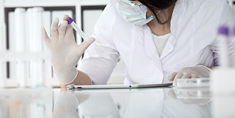 Close-up of professional female scientist in protective eyeglasses making experiment with reagents in laboratory or making blood tests. Medicine, science and research concept