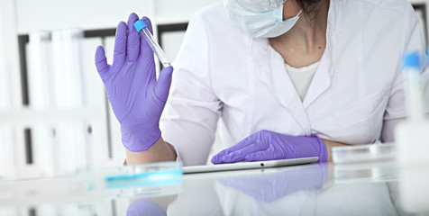 Close-up of professional female scientist in protective eyeglasses making experiment with reagents in laboratory or making blood tests. Medicine, science and research concept
