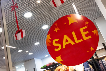 Red advertising sticker with the word SALE on the supermarket showcase in the clothing department. concept of holiday discounts and shopping.