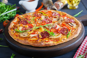 Fresh Italian pizza with chicken fillet, mushrooms, ham, salami, tomatoes, cheese on a black background. Italian food.
