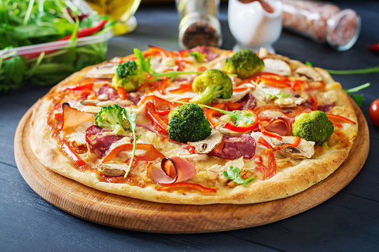 Fresh italian pizza with chicken fillet, mushrooms, ham, salami, tomatoes, broccoli, cheese on on black  background. Italian food.