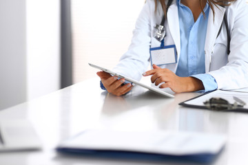 Unknown doctor woman using tablet computer while standing straight near window in hospital, close-up of hands. Medicine and health care concept
