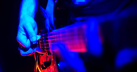 Plakat Rock concert. Guitarist plays the guitar. The guitar illuminated with bright neon lights. Hand close up