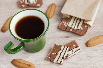 Green cup of americano and milk chocolate bar on wooden background