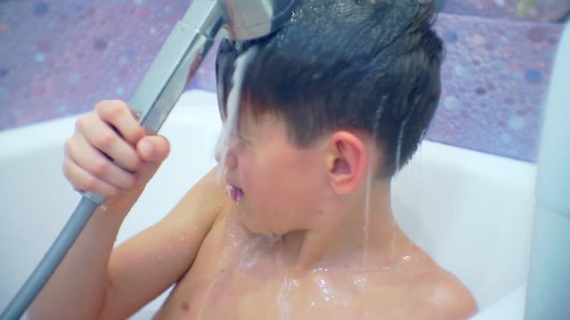 boy washes himself out of the shower while sitting in the bath