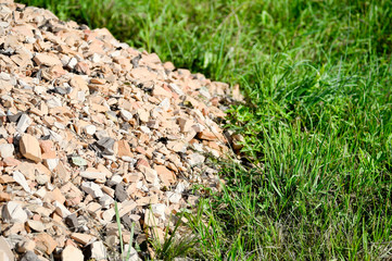 A pile of broken red brick with beige brick mixed in on a background of green grass. A contrasting background