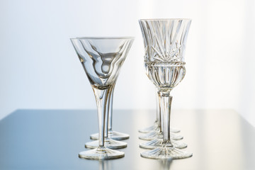 Decoration setup of wine and martini glasses set up in rows on a reflective table top.