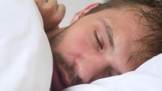 sick young man with fever asleep in bed, covered by a blanket