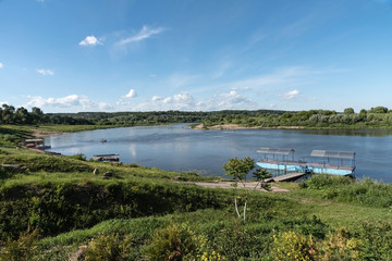 Colorful landscape, river with a deserted pier. View from the hill. Away from the coast of the boat, the beach. On the horizon is a forest, rural houses. Summer, sunny.